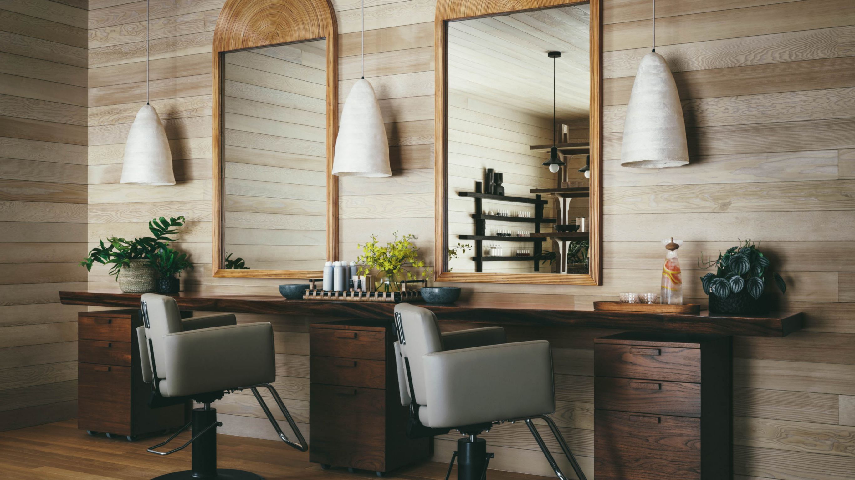 A hair salon with wooden walls, chairs,  mirrors, and pendant lights.